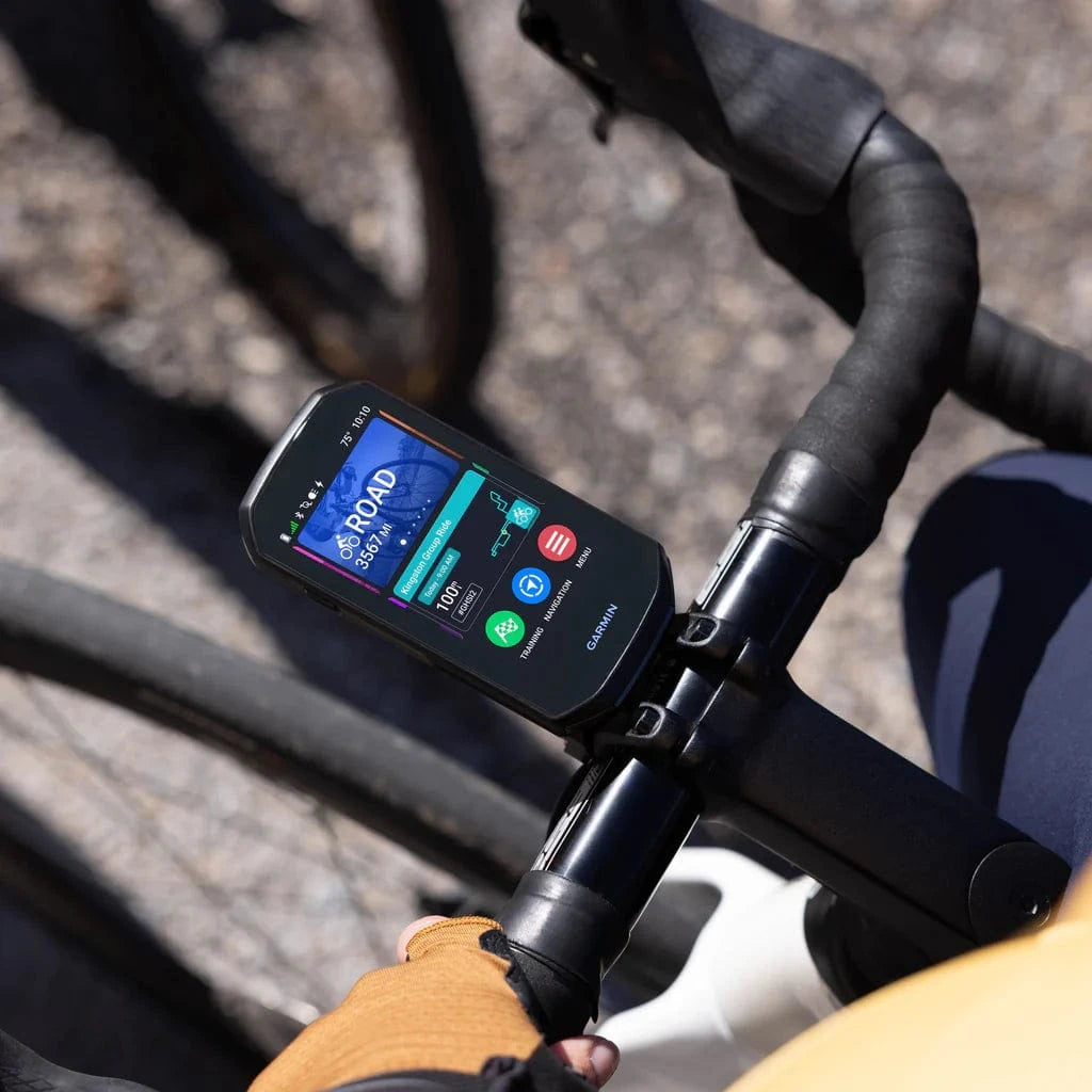 Close-up of a Garmin Edge 1050 cycling computer mounted on a road bike, displaying navigation and performance metrics, with a cyclist’s gloved hand gripping the handlebars