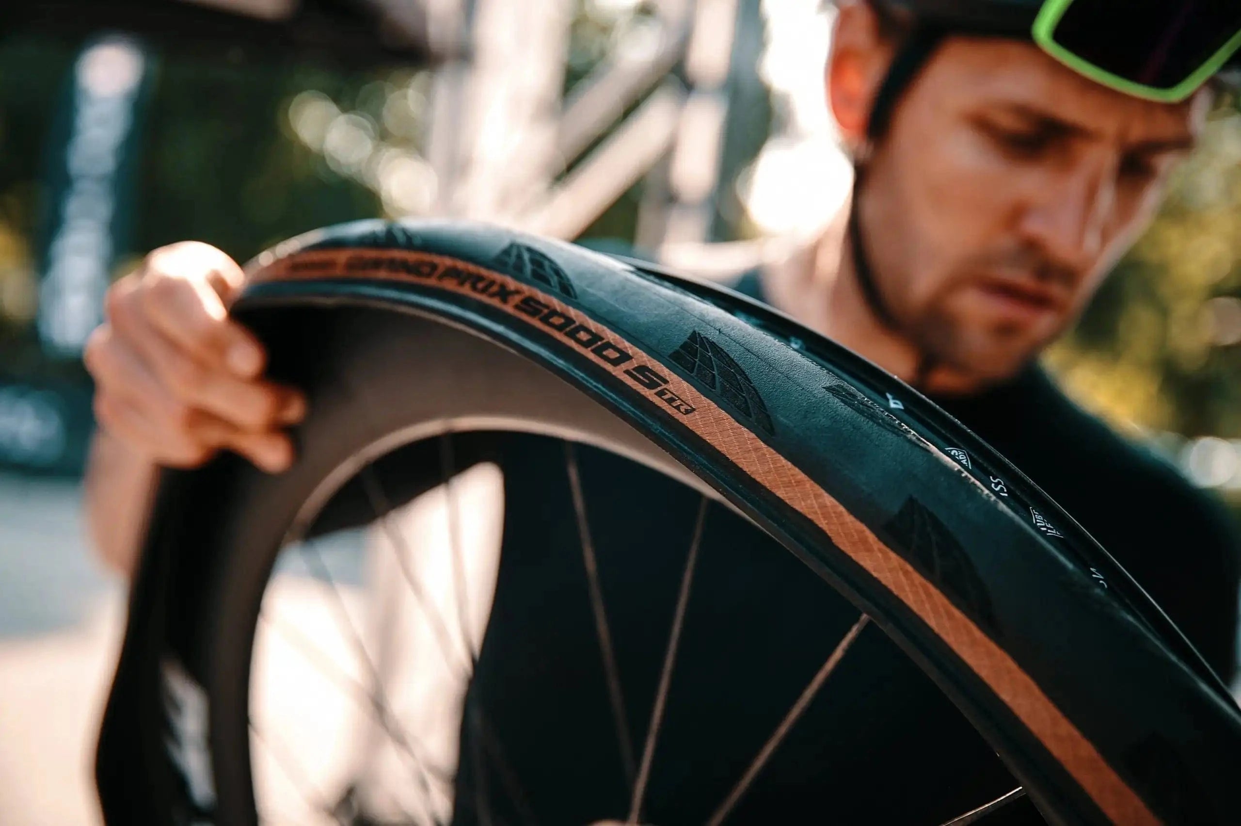 Close-up of a cyclist inspecting a Continental Grand Prix 5000 S TR tire with a tan sidewall, mounted on a deep carbon rim