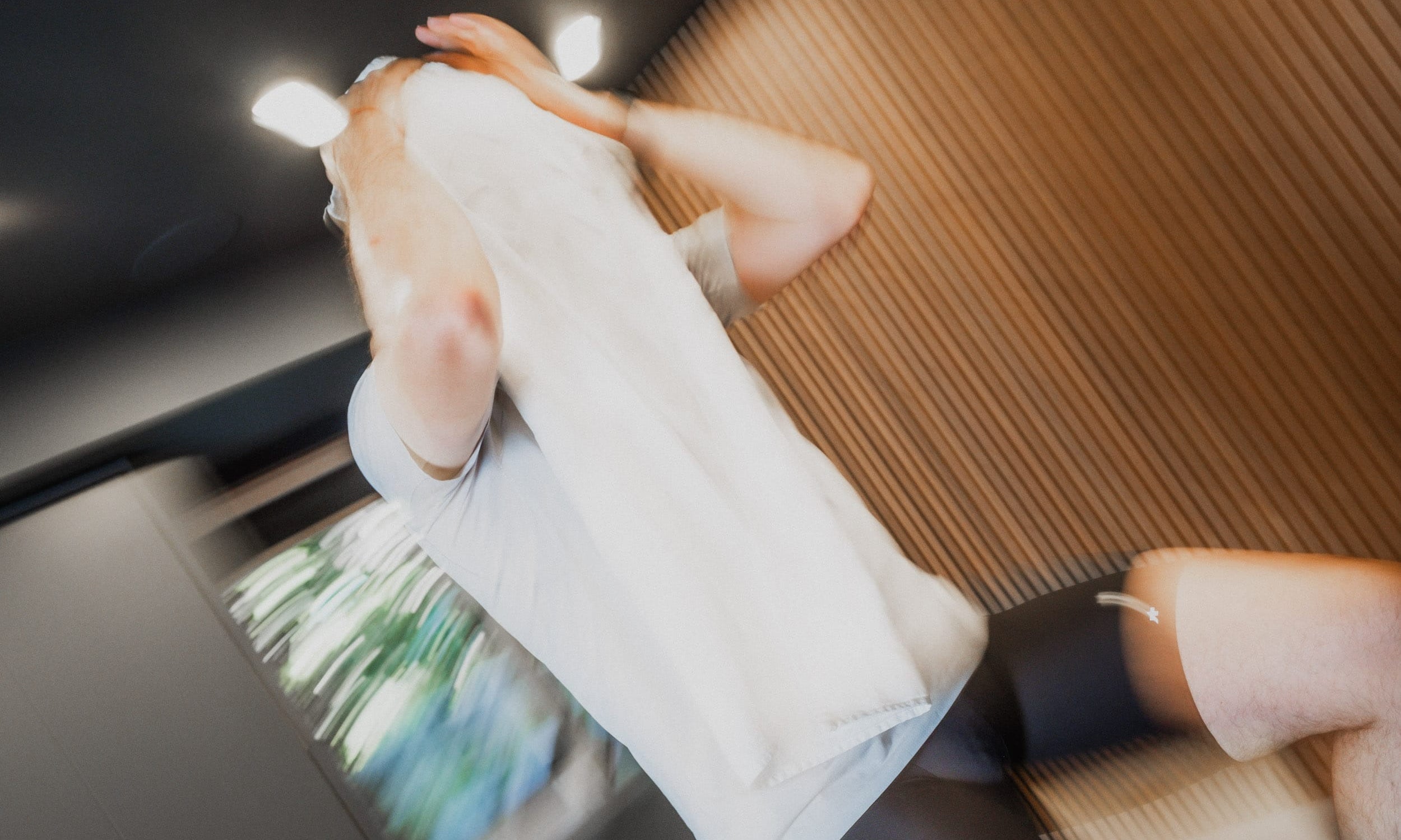 A person lying down on a bed or sofa, wearing a white t-shirt and black shorts, with a wooden slatted headboard behind them.