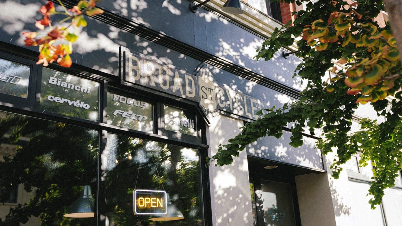 Storefront with 'Broad St Cycle' sign, surrounded by trees and hanging plants.