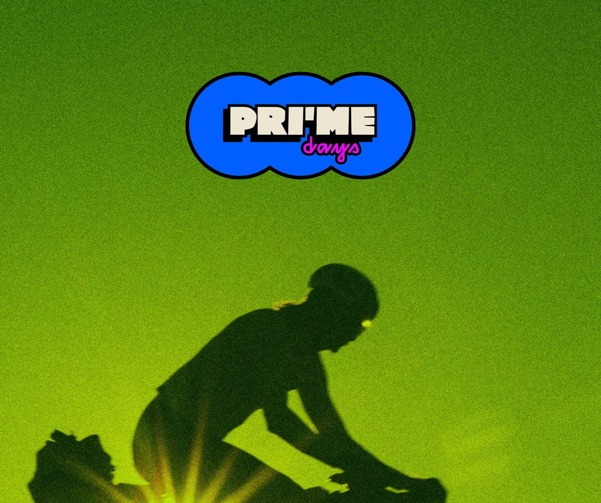 A mountain bike silhouette at sunset with a bright sun flare behind the rider, set against a green-yellow gradient background. A blue cloud-shaped logo at the top reads 'PRIME' with 'Bauya' underneath.