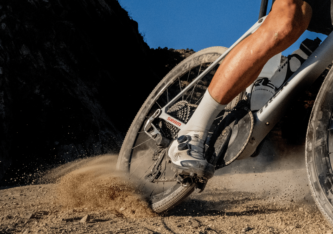 Person riding a mountain bike on a dirt trail with a clear blue sky.