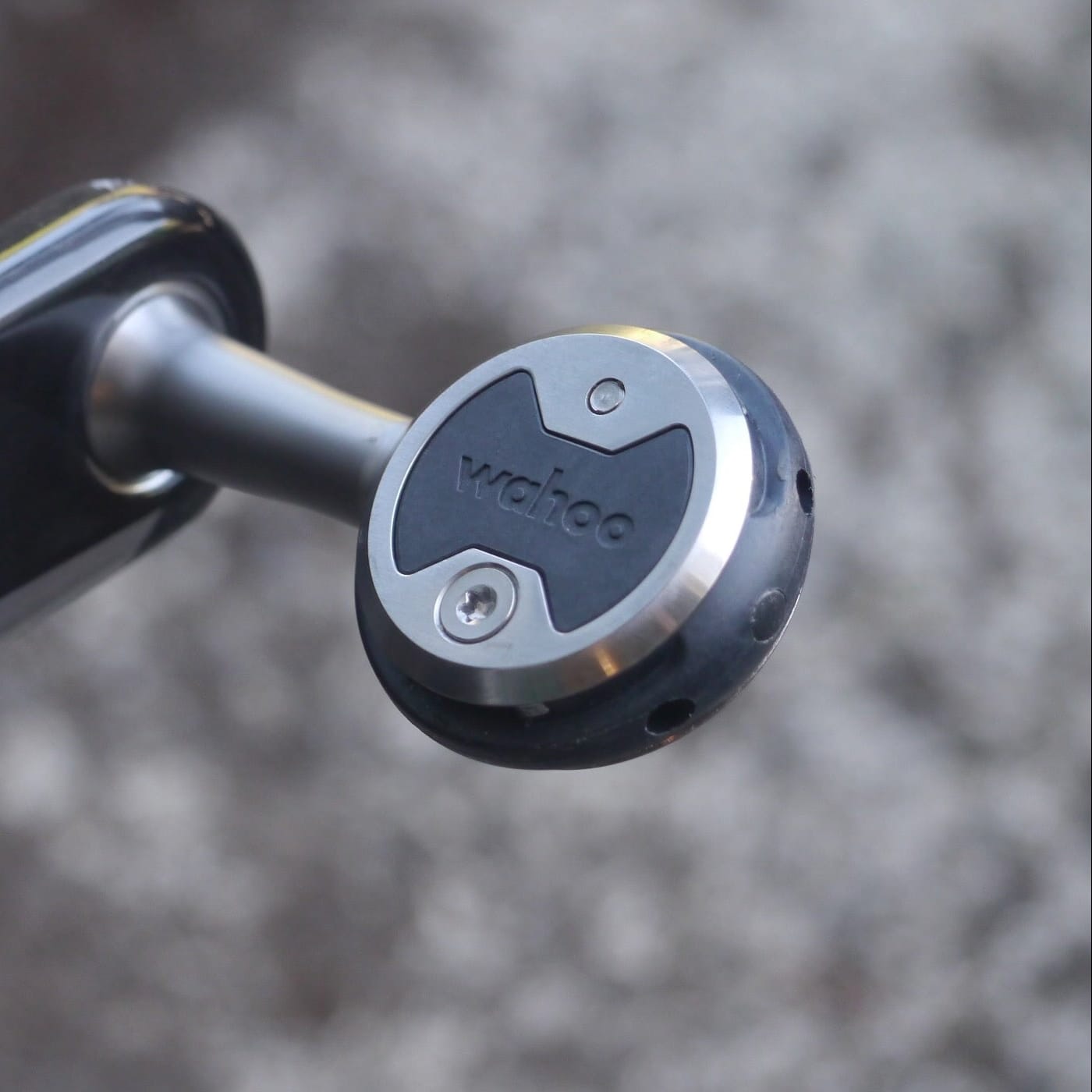 A close-up shot of a Wahoo heart rate sensor attached to a black and silver bicycle crank arm, set against a blurred gray outdoor background.